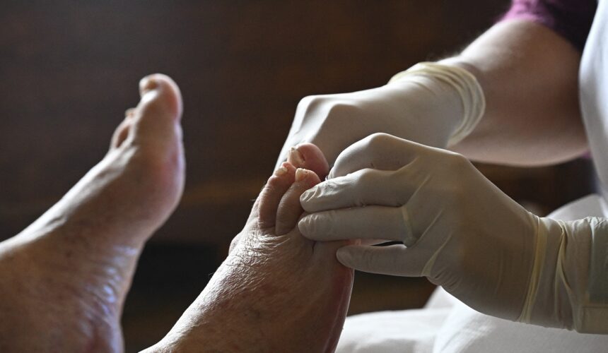 Une aide-soignante soigne le pied d’une personne âgée lors d’une visite à domicile, reflet du besoin croissant de soutien médical à domicile pour les personnes agées. Paris. 17 octobre 2025. Photo : Eric Beracassat / Hans Lucas via AFP